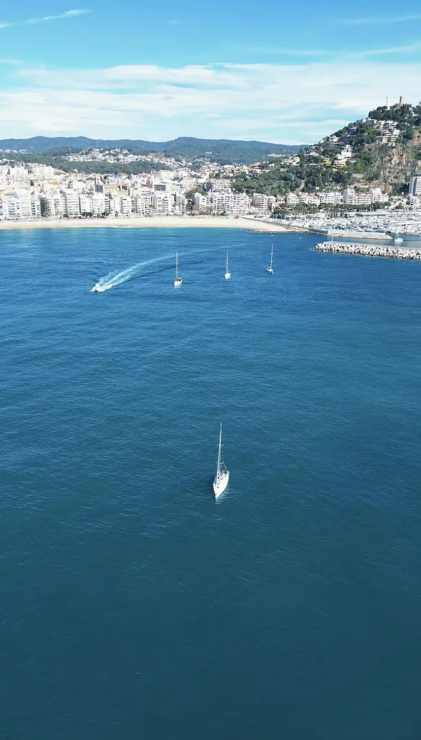Velero navegando frente a una localidad costera, fotografiado desde el aire