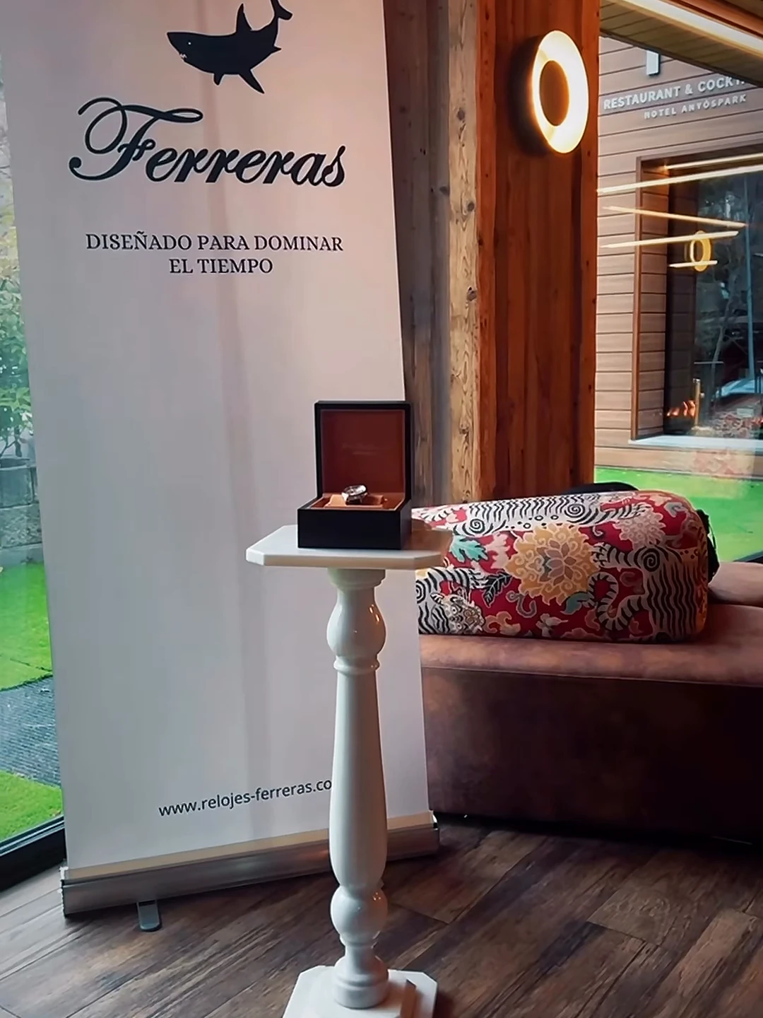 Expositor de Relojes Ferreras con el lema Diseñado para dominar el tiempo, en una presentación con estuches de reloj expuestos y embarcaciones al fondo